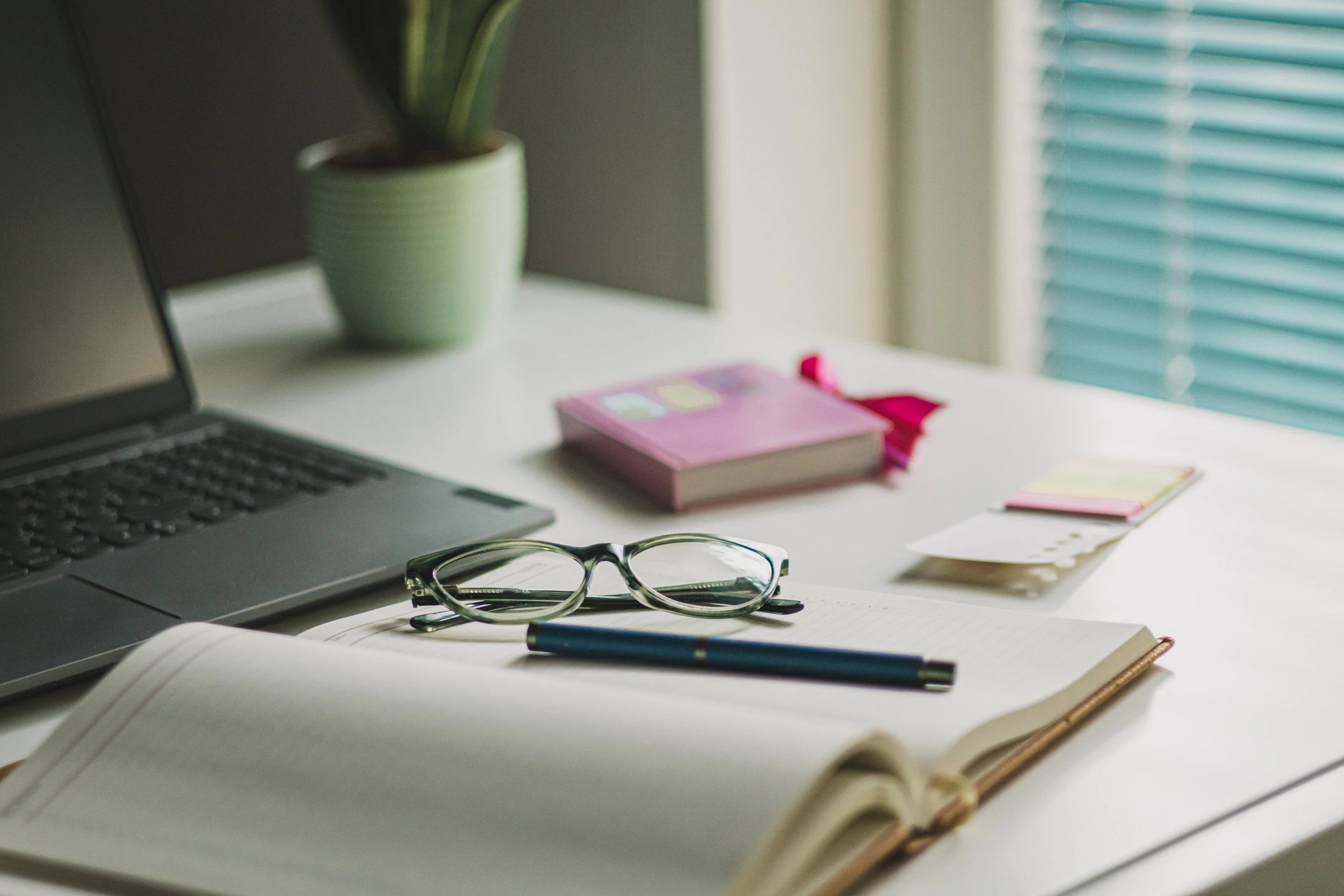 Writing desk with laptop, coffee, glasses, and notebook